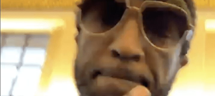 Person wearing sunglasses indoors, blurred background.